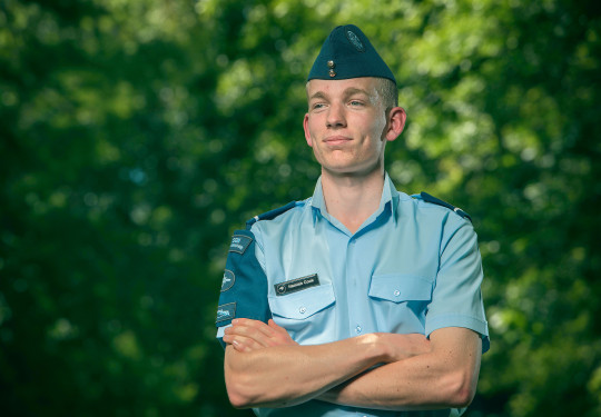 Cadet Warrant Officer Hamish Cook stands smiling, looking away form the camera with greenery in the background.