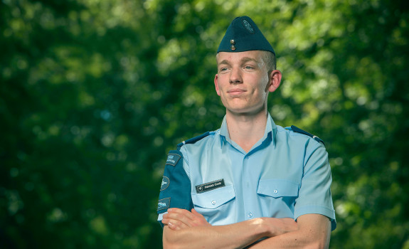 Cadet Warrant Officer Hamish Cook stands smiling, looking away form the camera with greenery in the background.