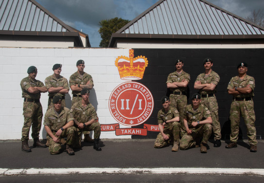 Soldiers from 2/1 RNZIR stand are ready for Exercise Cambrian Patrol after completing preparation training at Burnham Military Camp in front of their unit logo.