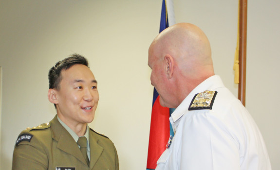Captain Jin Cha in military dress uniform, receives the New Zealand Defence Service Medal from Commander Joint Forces New Zealand, Rear Admiral Jim Gilmour. The pair shake hands.