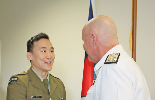 Captain Jin Cha in military dress uniform, receives the New Zealand Defence Service Medal from Commander Joint Forces New Zealand, Rear Admiral Jim Gilmour. The pair shake hands.