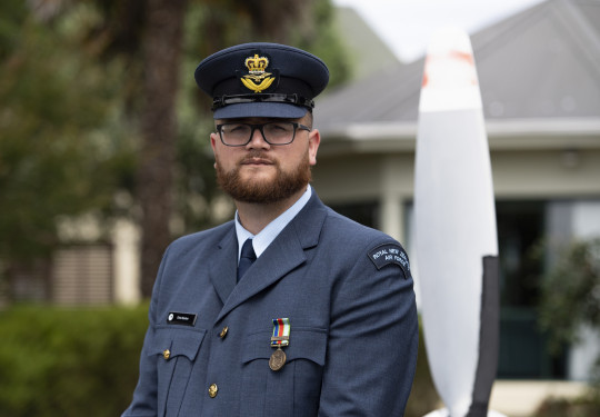 An airman in uniform stands looking at the camera with their hat on. 