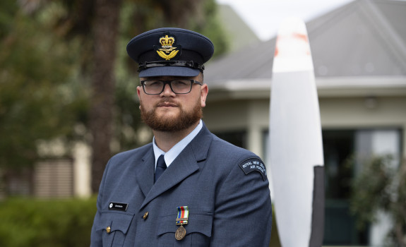 An airman in uniform stands looking at the camera with their hat on.