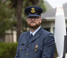 An airman in uniform stands looking at the camera with their hat on. 