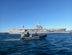 A small Royal New Zealand Navy Rigid Hull Inflatable Boat in front of the large grey US Navy ship, USS Blue Ridge.
