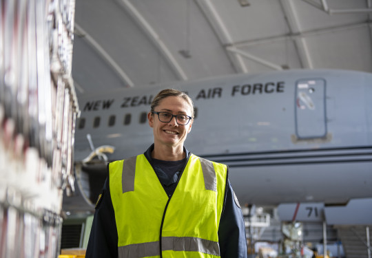 Group Captain Susie Barns stands smiling in a high vis vest with a Boeing aircraft in the background.