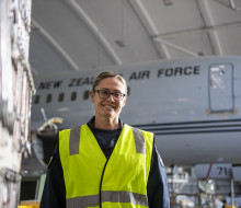 Group Captain Susie Barns stands smiling in a high vis vest with a Boeing aircraft in the background.