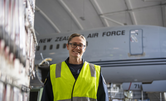 Group Captain Susie Barns stands smiling in a high vis vest with a Boeing aircraft in the background.