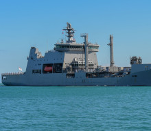 Large grey tanker ship with orange life boats slowly passes land as it arrives into Pearl Harbour.