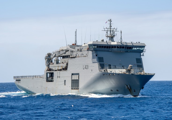 A large grey ship sails through blue water under clear skies,