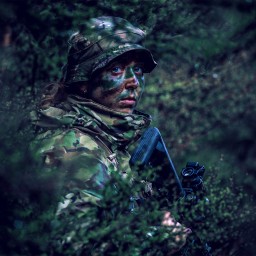 Female soldier standing camouflaged in bush.