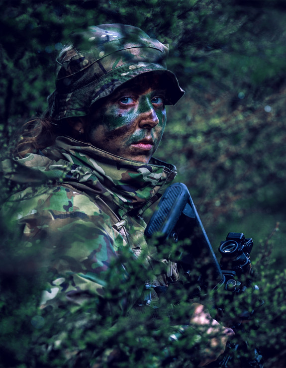 Female soldier standing camouflaged in bush.