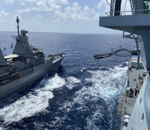 A photo of HMNZS Te Kaha receiving fuel from RFA Tidespring - photo is taken in the wide ocean on a sunny day. There are some clouds in the sky. 