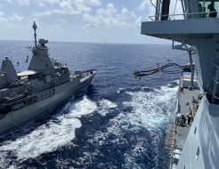 A photo of HMNZS Te Kaha receiving fuel from RFA Tidespring - photo is taken in the wide ocean on a sunny day. There are some clouds in the sky. 