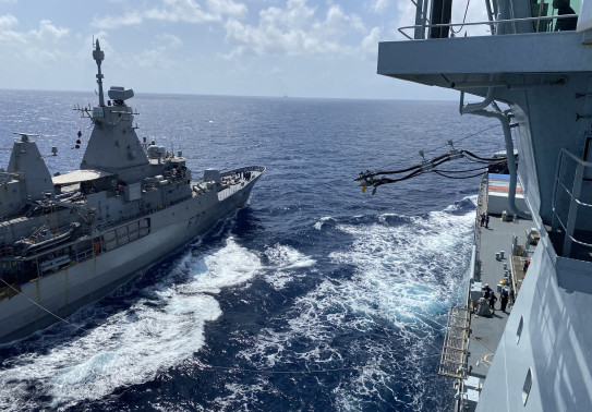 A photo of HMNZS Te Kaha receiving fuel from RFA Tidespring - photo is taken in the wide ocean on a sunny day. There are some clouds in the sky. 