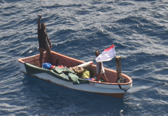 Two people on a small boat who went missing in Kiribati waters waving to camera (on aircraft)  RNZAF P-3K2 Orion following a two-day search.