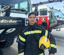 Royal New Zealand Air Force firefighter Leading Aircraftman Te Waiora Pirikahu poses in front of Andersen Air Force Base fire appliances