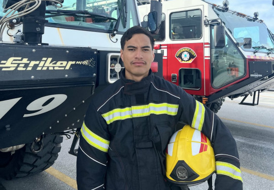 Royal New Zealand Air Force firefighter Leading Aircraftman Te Waiora Pirikahu poses in front of Andersen Air Force Base fire appliances