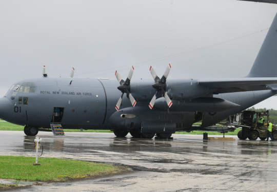 A Royal New Zealand Hercules aircraft on the tarmac at the airport in Tonga. Air Force personnel are removing supplies from the aircraft