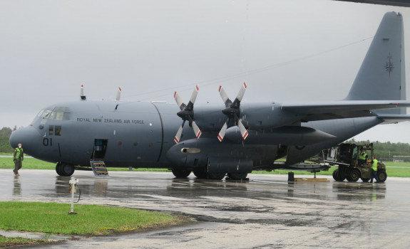 A Royal New Zealand Hercules aircraft on the tarmac at the airport in Tonga. Air Force personnel are removing supplies from the aircraft