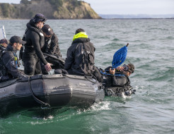 A diver from HMNZS Matataua leaves a Zodiac, a small boat. Five other sailors and divers remain in the boat.