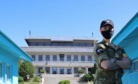 Flight Lieutenant Emily Hall standing in uniform and a mask with her arms crossed in front of various buildings