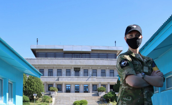 Flight Lieutenant Emily Hall standing in uniform and a mask with her arms crossed in front of various buildings