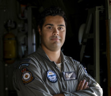 An aviator stands armed crossed looking at the camera in a flying suit.