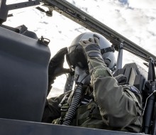 An Air Force pilot adjusts his helmet eye protection as he sits in the cockpit of a small aircraft.