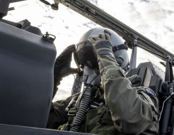 An Air Force pilot adjusts his helmet eye protection as he sits in the cockpit of a small aircraft.