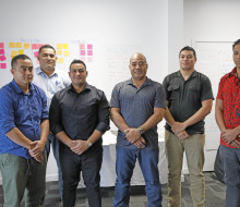 A group of people stand in a line for the photo in a classroom with brainstorming post-it notes in the background