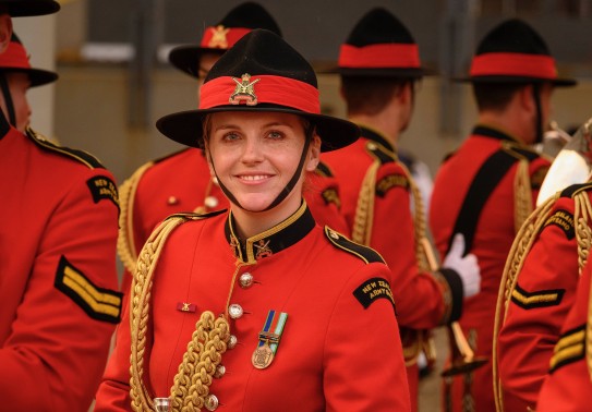 A NZ Army band member smiles to the camera while other members of the band are facing away in the background.