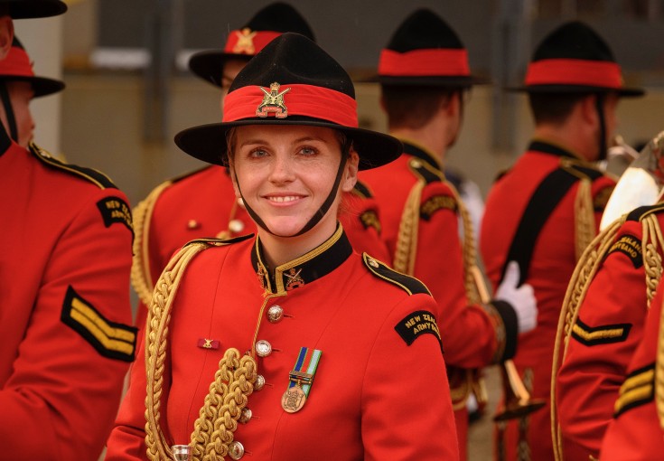 A NZ Army band member smiles to the camera while other members of the band are facing away in the background.