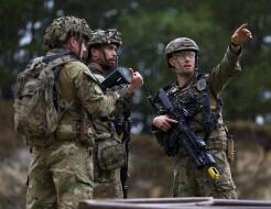 Three soldiers in Army uniform holding weapons having a discussion. The solider on the right points into the distance.