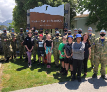 The officer cadets with some of the students and staff from Wairau Valley School. The uniformed personnel have masks on and it is a sunny day.