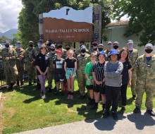 The officer cadets with some of the students and staff from Wairau Valley School. The uniformed personnel have masks on and it is a sunny day.