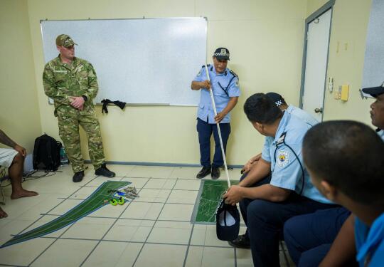 A planning meeting with people in various uniforms looking at a map on tiled flooring in a small room