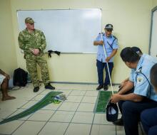 A planning meeting with people in various uniforms looking at a map on tiled flooring in a small room