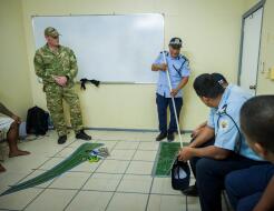 A planning meeting with people in various uniforms looking at a map on tiled flooring in a small room