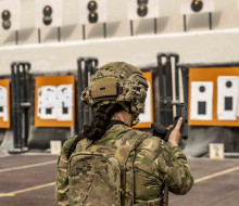 A member of the Female Engagement Team wearing full Army uniform including a helmet reloads a pistol on the weapon range.