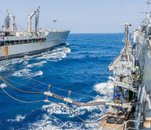 Two large grey ships sail across blue seas only 45m away from each other. They are connected by lines and fuels pipes. 