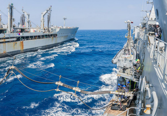 Two large grey ships sail across blue seas only 45m away from each other. They are connected by lines and fuels pipes. 