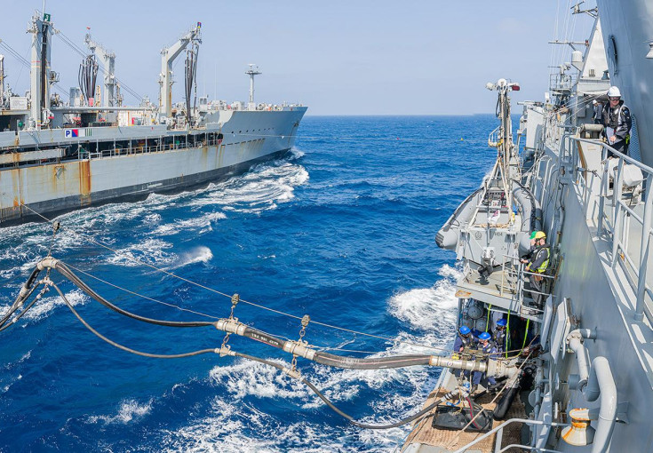 Two large grey ships sail across blue seas only 45m away from each other. They are connected by lines and fuels pipes. 