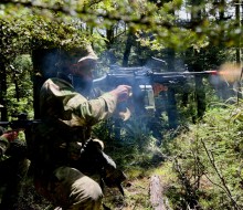 Two soldiers fires a weapons in dense bush.
