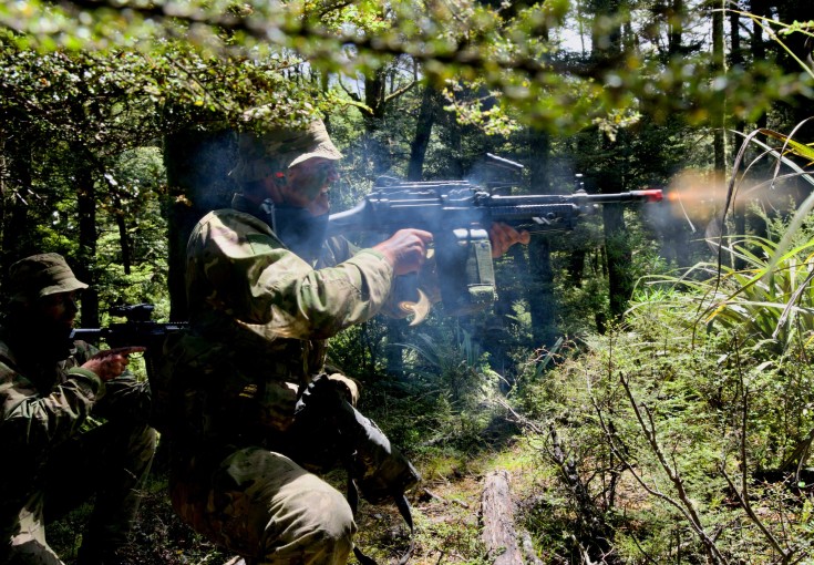 Two soldiers fires a weapons in dense bush.