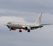 Side view of a P-8A Poseidon, a large grey jet aircraft with landing gear down as the plane prepares to land on a cloudy day.
