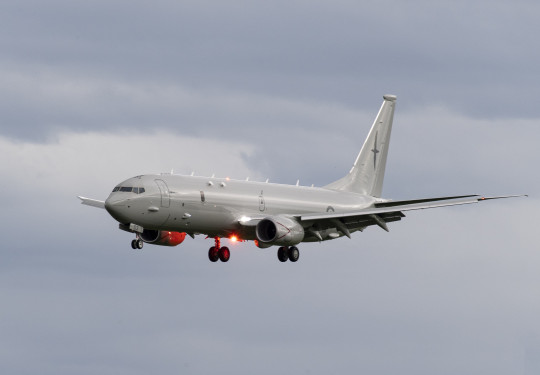 Side view of a P-8A Poseidon, a large grey jet aircraft with landing gear down as the plane prepares to land on a cloudy day.