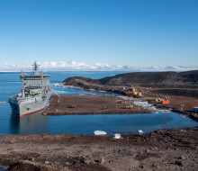 HMNZS Aotearoa and crew have berthed at Antarctica, delivering supplies and providing key support. It's a sunny day, blue sky.