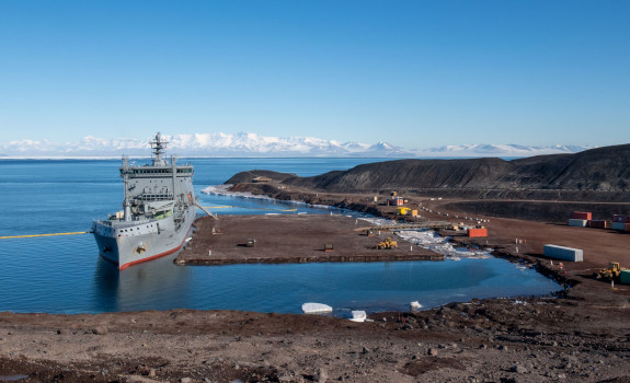 HMNZS Aotearoa and crew have berthed at Antarctica, delivering supplies and providing key support. It's a sunny day, blue sky.