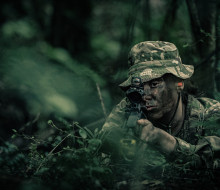 Private Zara Reid looks down the scope of a rifle in full camouflage as she takes part in regular training with Wellington Company, 5/7 Battalion, RNZIR